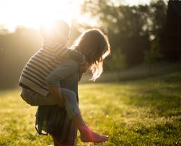 Parent carrying child through grassy field, emphasizing outdoor tick exposure and Lyme disease health risks.