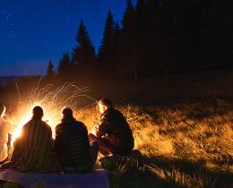 Five people sitting around a glowing campfire under a starry night sky, surrounded by trees—evoking the ancient tradition of storytelling in community.