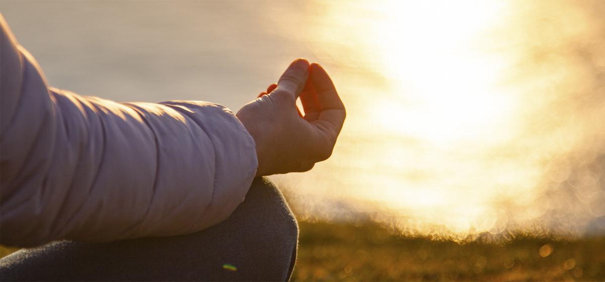 Person meditating outside at sunrise at the lakeshore