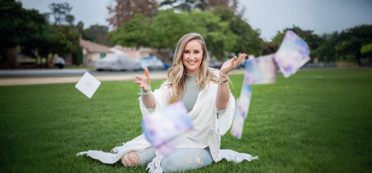 Candace Dalton sitting in a field with a whirlwind of tarot cards around her