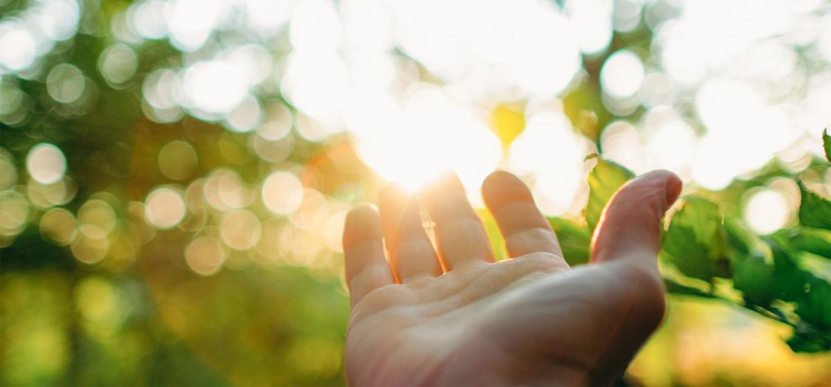 Person reaching hand out to sun