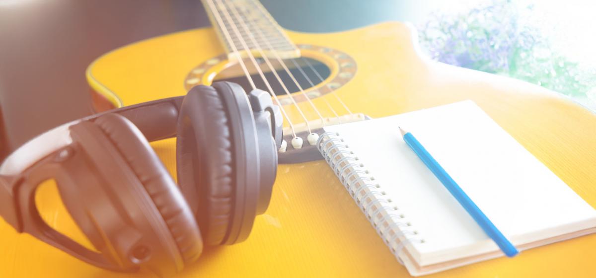 Acoustic guitar, headphones, and notepad in a songwriting session