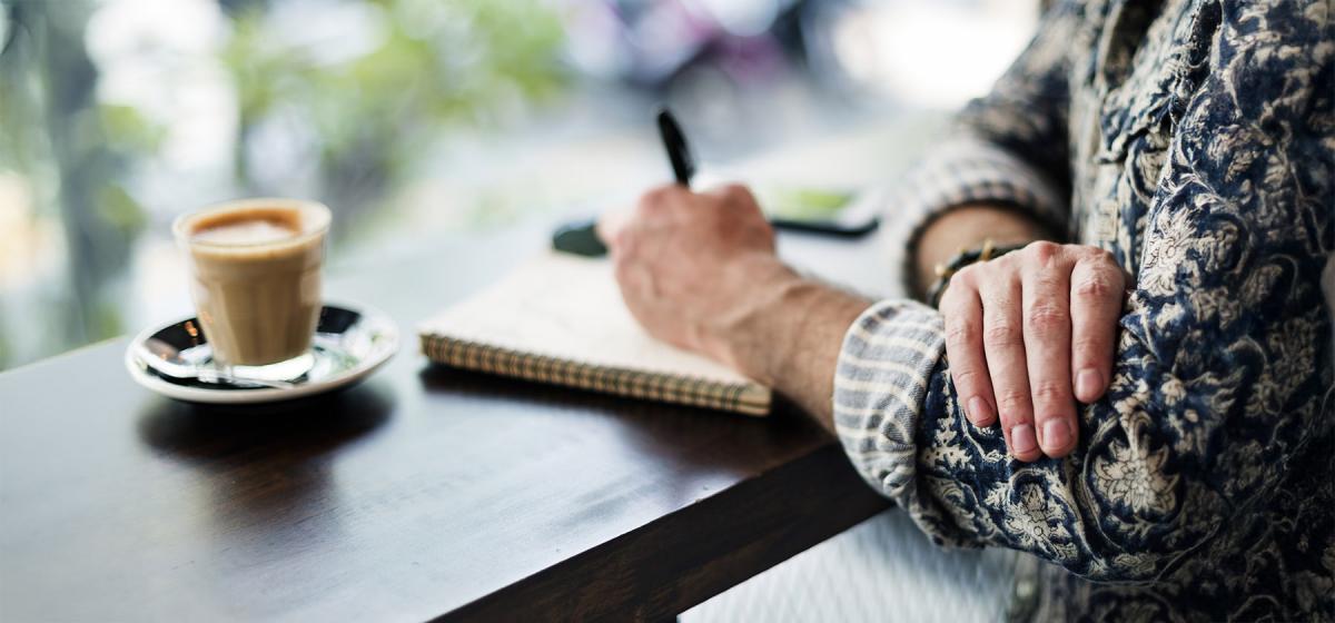 Author writing at a table with a cup of coffee