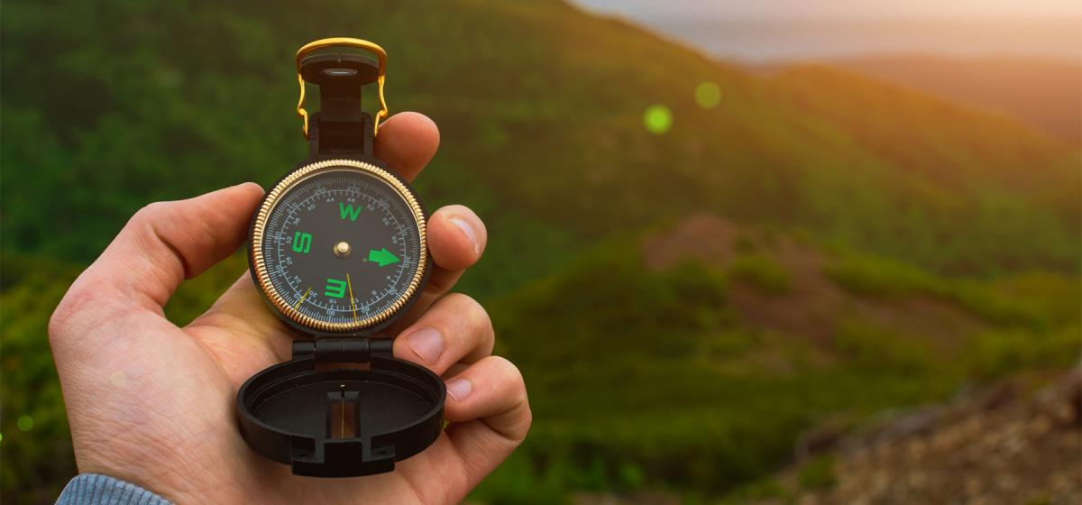 Person holding compass up in the forest, showing the Four Directions