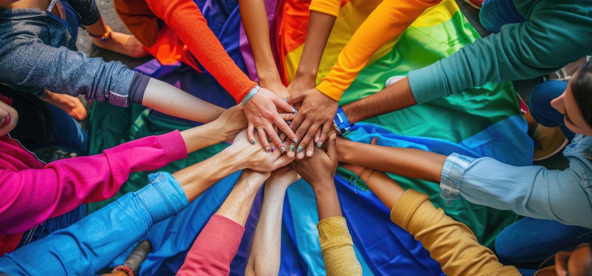 Group of people in brightly colored shirts forming a rainbow