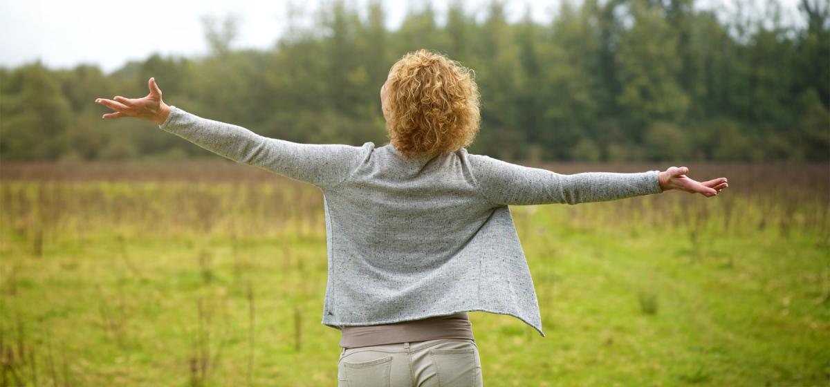 Woman with arms open wide looking out into a forest