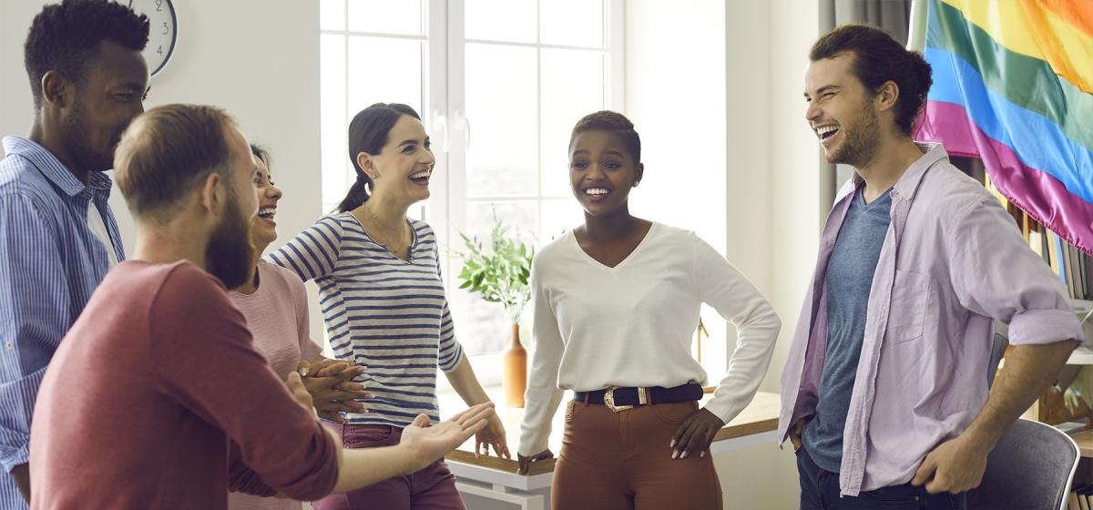 Group of people in storytelling session, with rainbow flag hanging in the background