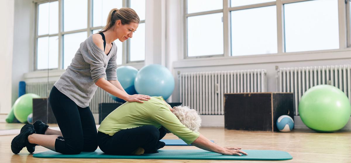 Yoga therapy practitioner helping an elderly woman stretch