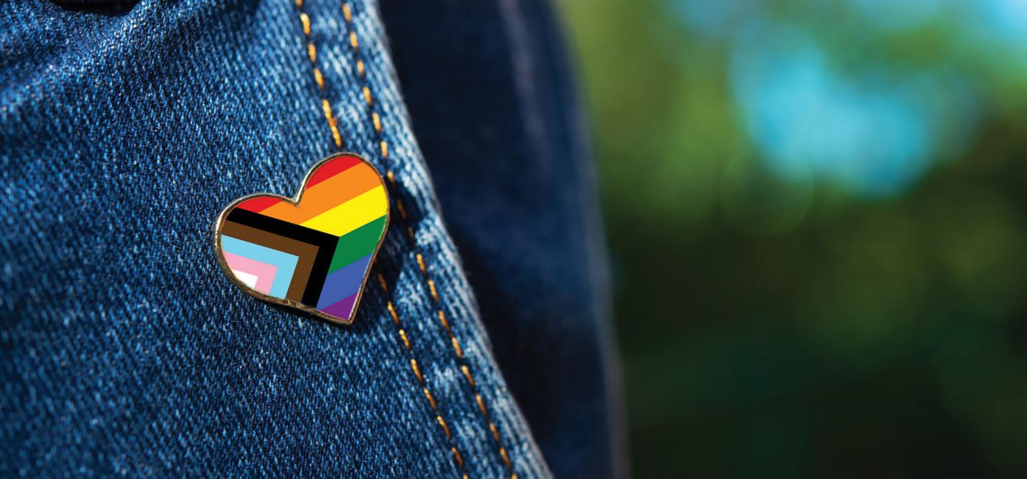 Closeup of denim jacket with inclusive Pride pin